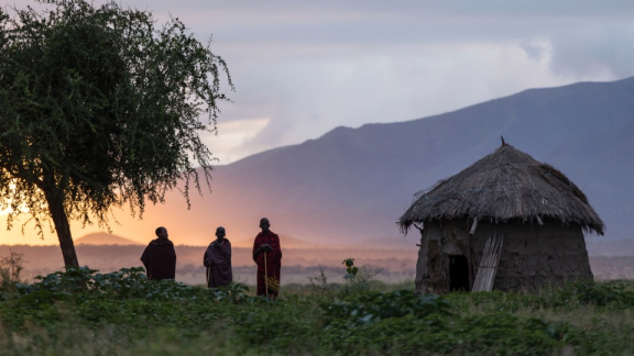 Drei Personen stehen bei Sonnenaufgang neben einer Hütte in Tansania
