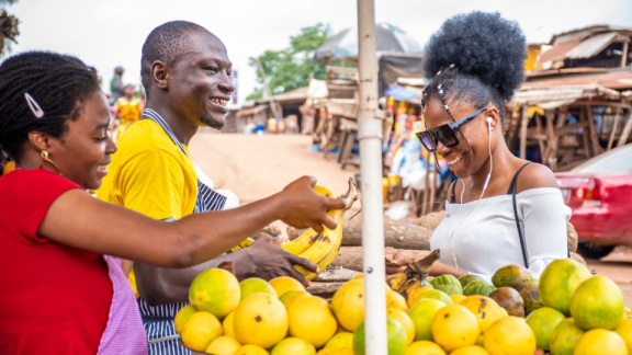 Drei Nigerianer stehen an einem Marktstand mit Bananen und Zitronen