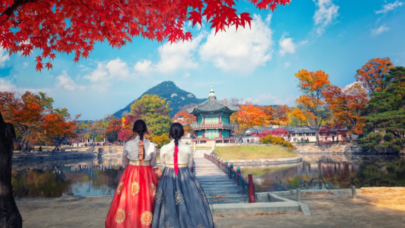 Zwei Frauen in Hanbok vor einem Pavillon und Herbstlandschaft in Südkorea