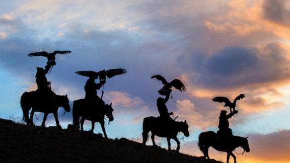 Silhouetten mongolischer Reiter mit Jagdadlern bei Sonnenuntergang in weiter Landschaft