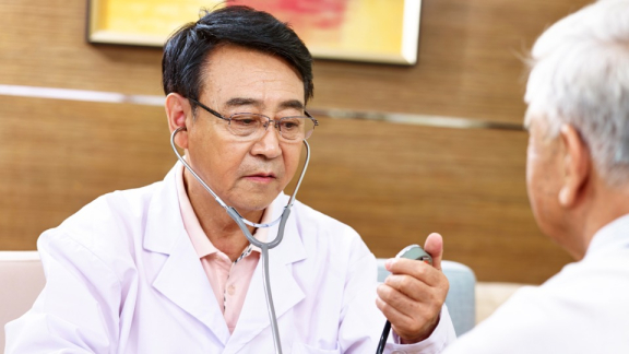 Ein Arzt aus Singapur misst die Werte eines älteren Patienten mit einem Stethoskop