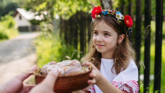 Ein kleines Mädchen in traditioneller slowakischer Tracht hält einen Korb mit Ostereiern