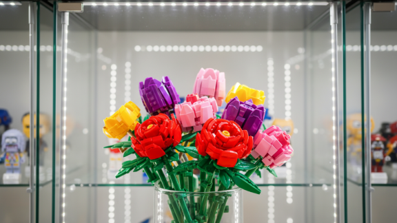 Ein bunter Klemmbaustein-Blumenstrauß in einer beleuchteten Glasvitrine mit Sammelfiguren vor der Transportsicherung durch DACHSER & KOLB.