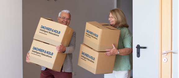 Älteres Paar trägt Umzugskartons in neues Zuhause – Seniorenumzug mit professionellem Relocationsservice.