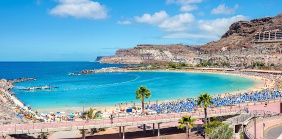 Bucht in Spanien mit Sandstrand, Palmen, türkisblauem Meer und felsiger Küstenlandschaft