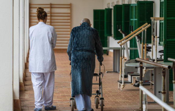 Pflegekraft begleitet ältere Person mit Rollator in einer medizinischen Einrichtung in Spanien