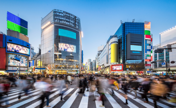 Belebte Kreuzung mit Hochhäusern und vielen Fußgängern in Tokio bei Abenddämmerung