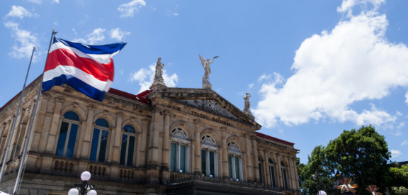 Flagge Costa Ricas vor historischem Theatergebäude unter blauem Himmel