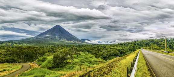Vulkan in Costa Rica mit Straße, Regenwald und bewölktem Himmel