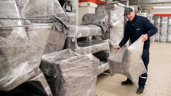 Mann trägt verpacktes Möbelstück. Umzugshelfer bei der Arbeit