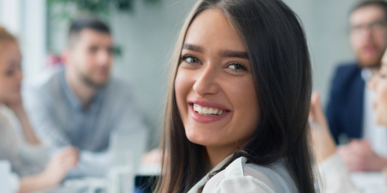 Eine lächelnde junge Frau im Vordergrund einer Gruppe während einer Ausbildungsveranstaltung.