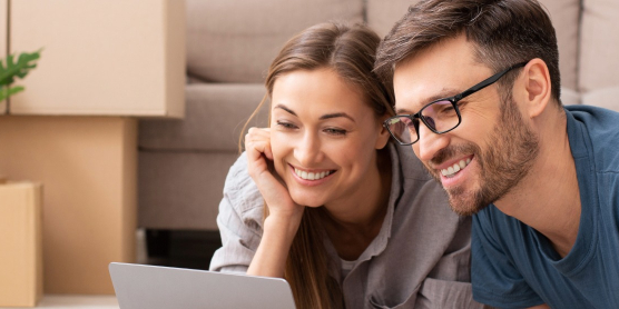Couple planning their move on a laptop in front of moving boxes in the living room