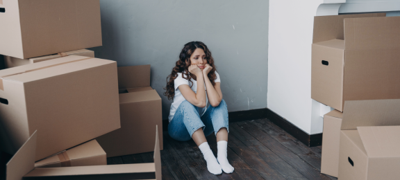 Junge Frau sitzt traurig zwischen Umzugskartons – Symbolbild für emotionale Belastung durch Umzugsdepression.