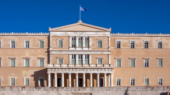 Griechisches Parlament in Athen mit Flagge vor klarem blauem Himmel
