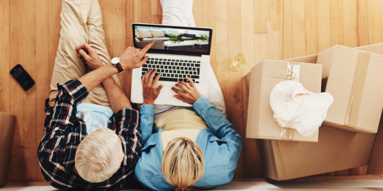 Älteres Paar berechnet Umzugskosten am Laptop, umgeben von Umzugskartons in neuer Wohnung