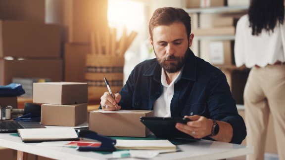 Mann mit Tablet und Frachtbrief (Bill of Lading) verpackt Päckchen für den Versand. E-Commerce und Logistik.