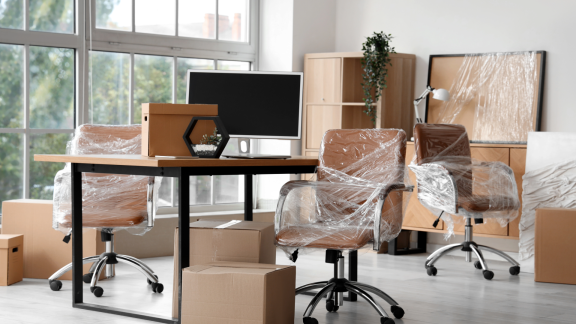 Büroraum mit verpackten Drehstühlen, Schreibtisch und Kartons, Emballage für Büroumzug