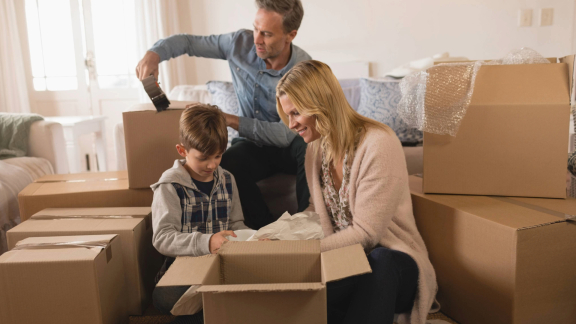 Eine Familie packt Umzugskartons in ihrem Zuhause aus oder ein. Kinder helfen beim