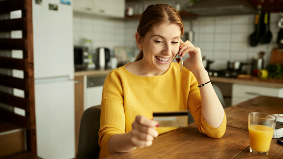 Smiling woman on phone holding a gold credit card. Symbolizes convenient moving with installment payments.