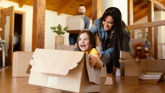 Happy family moving. Girl laughs in moving box, mother pushes, father carries boxes. Moving with installment payments.