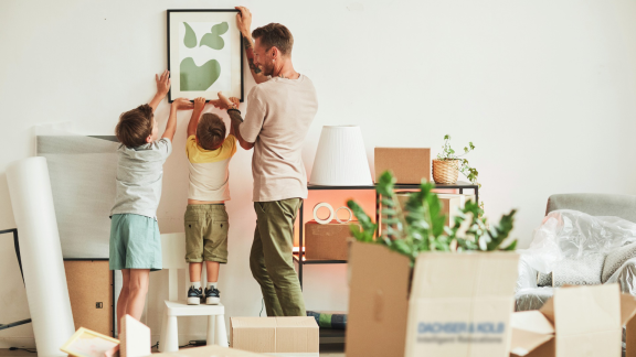 Family hanging picture in new home with moving boxes, moving on a budget