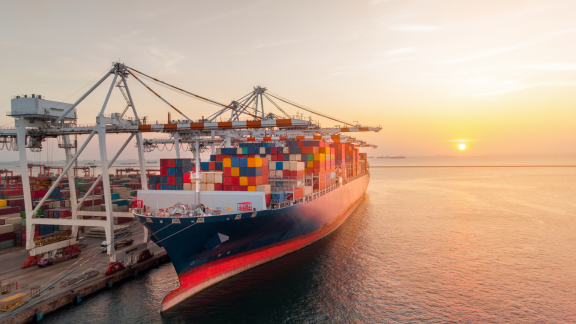 Containerschiff im POE (Port of Entry) beim Entladen im Einfuhrhafen bei Sonnenuntergang über dem Meer.