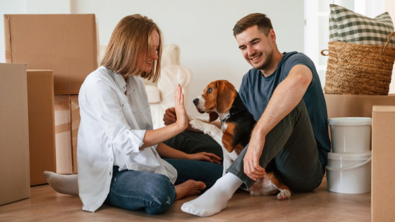 Paar mit Hund zwischen Umzugskartons – Kurzleitfaden für den stressfreien Umzug mit Hund oder Kleintier.