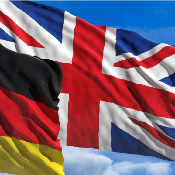 German and UK flags waving side by side against a blue sky, symbolizing customs from the UK to Germany