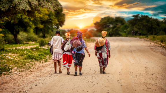 Landstraße in Südafrika, auf der vier Personen Richtung untergehende Sonne laufen